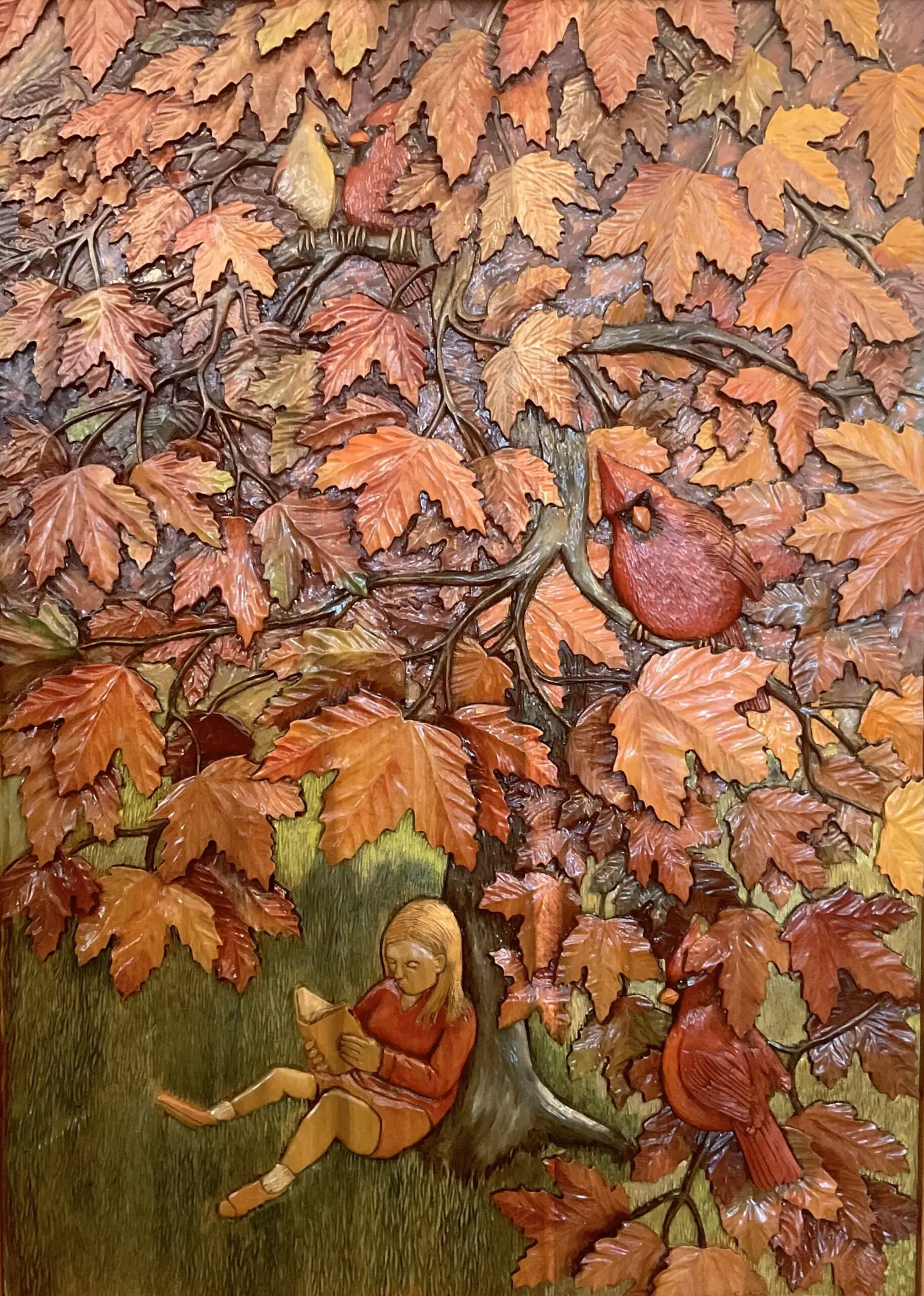Gary Cota's hand-carved, painted wood relief of a girl reading under an autumn tree filled with red and orange leaves and cardinals