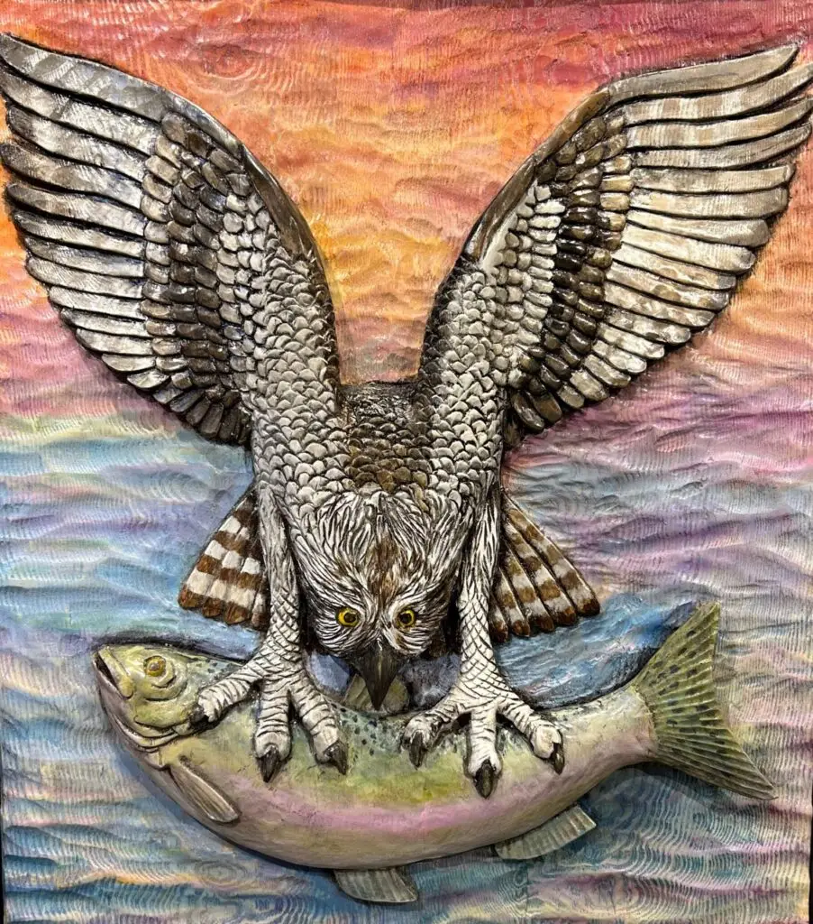 Painted wood carving of an osprey gripping a fish with its talons, wings spread wide as it prepares to fly from the water.