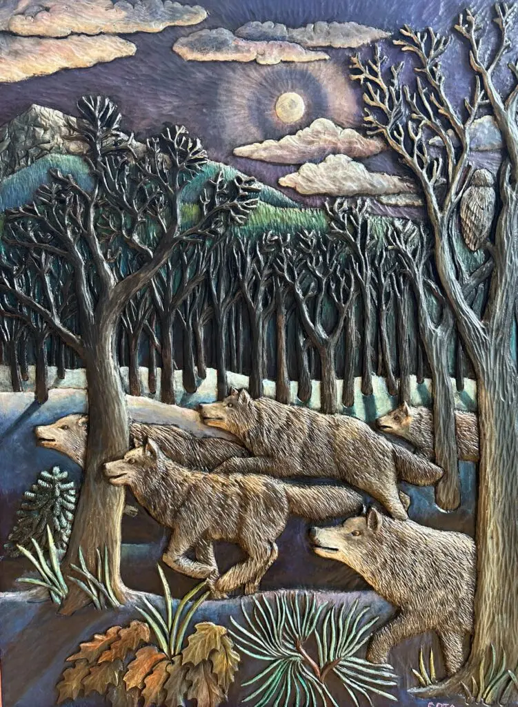 Award-winning wood carving by Gary Cota depicting a pack of wolves moving silently through a moonlit winter forest. Bare trees frame the scene, while a full moon, distant mountains, drifting clouds, and a watchful owl create a dramatic atmosphere that captures the beauty and mystery of the wild.