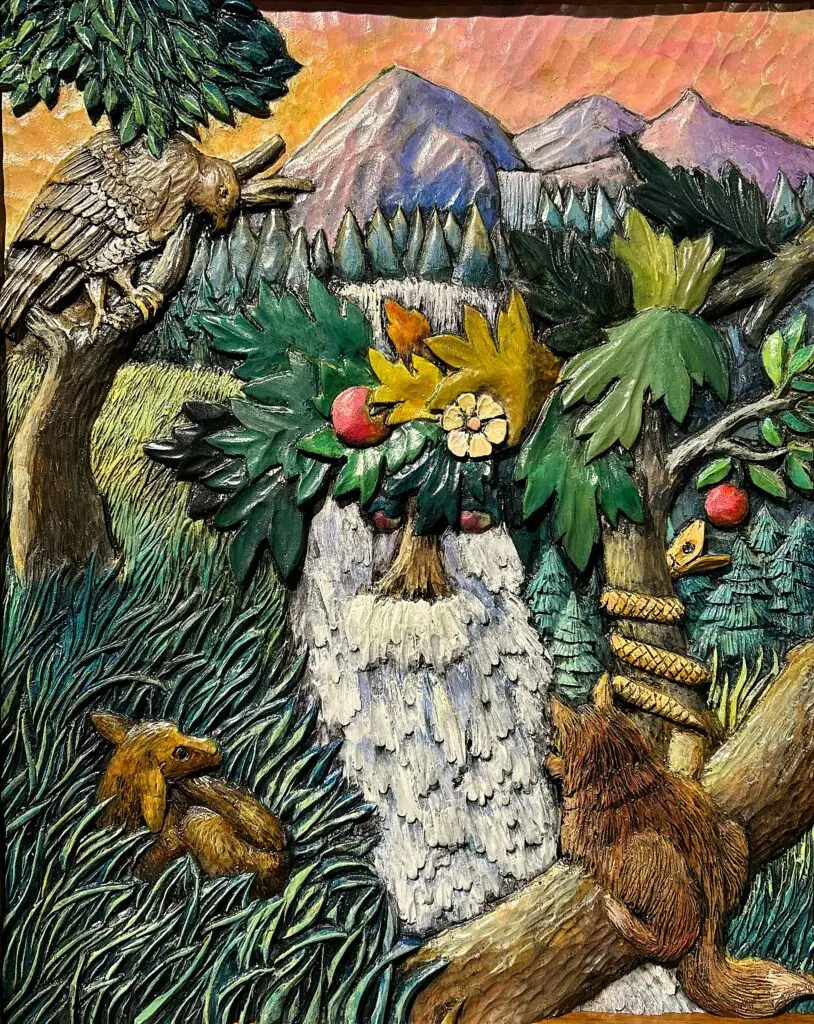 Perception by Gary Cota, an intricately carved and painted wood relief depicting an old bearded man emerging from a forest landscape, with an owl, squirrel, snake, and fox hidden among trees, mountains, and a waterfall.